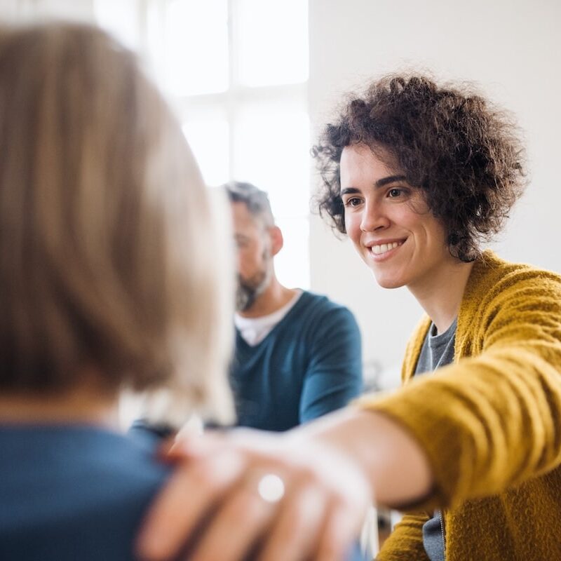 Men and women sitting in a circle during group therapy, supporting each other.
